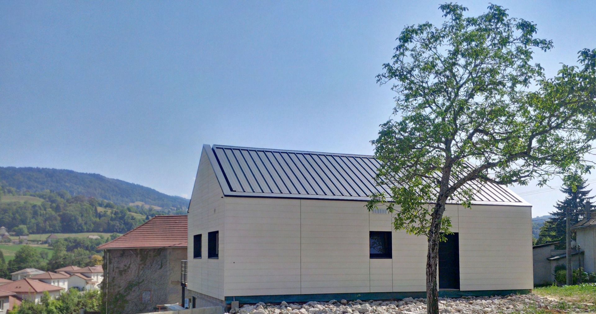 Kleines modernes Haus mit schwarzen Fenstern. Als Fassade kam eine Holzfassade in der Farbe creme zum Einsatz.