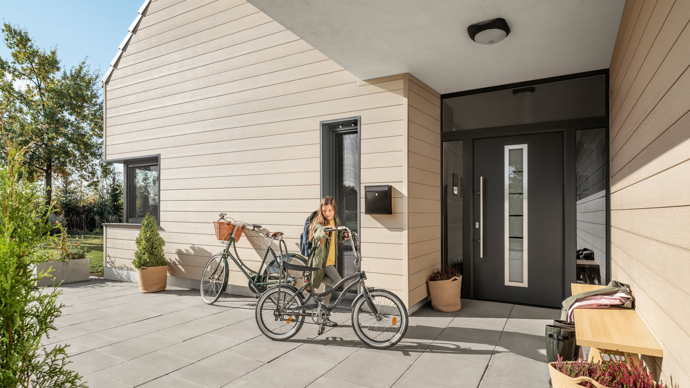 Idee zu Fassadenverkleidung in der Farbe beige. Die Fenster und die Tür sind in dunkelgrau abgesetzt.