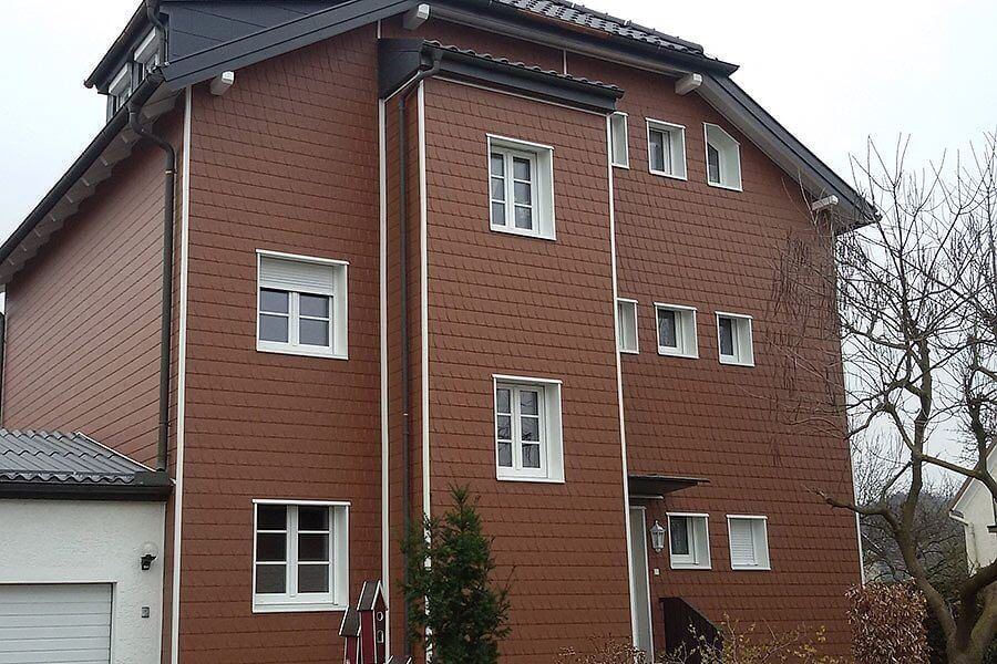 Rote Schieferstrukturfassade. Die Fenster sind weiß abgesetzt.