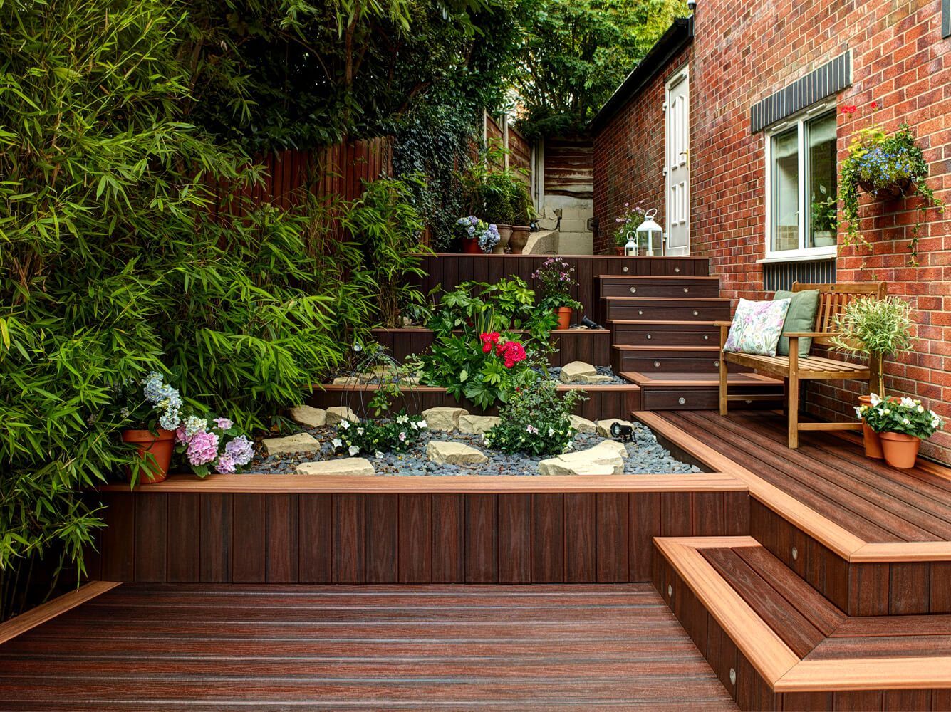 Rote WPC Terrasse mit Treppen und kleinen Garten auf unterschiedlichen Ebenen.
