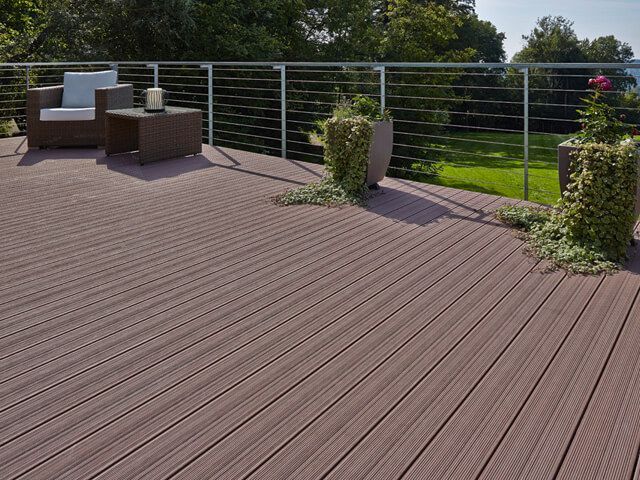 Braune Terrasse erhöht vor einer Gartenlandschaft mit einem Metallgeländer und Sitzmöbeln.