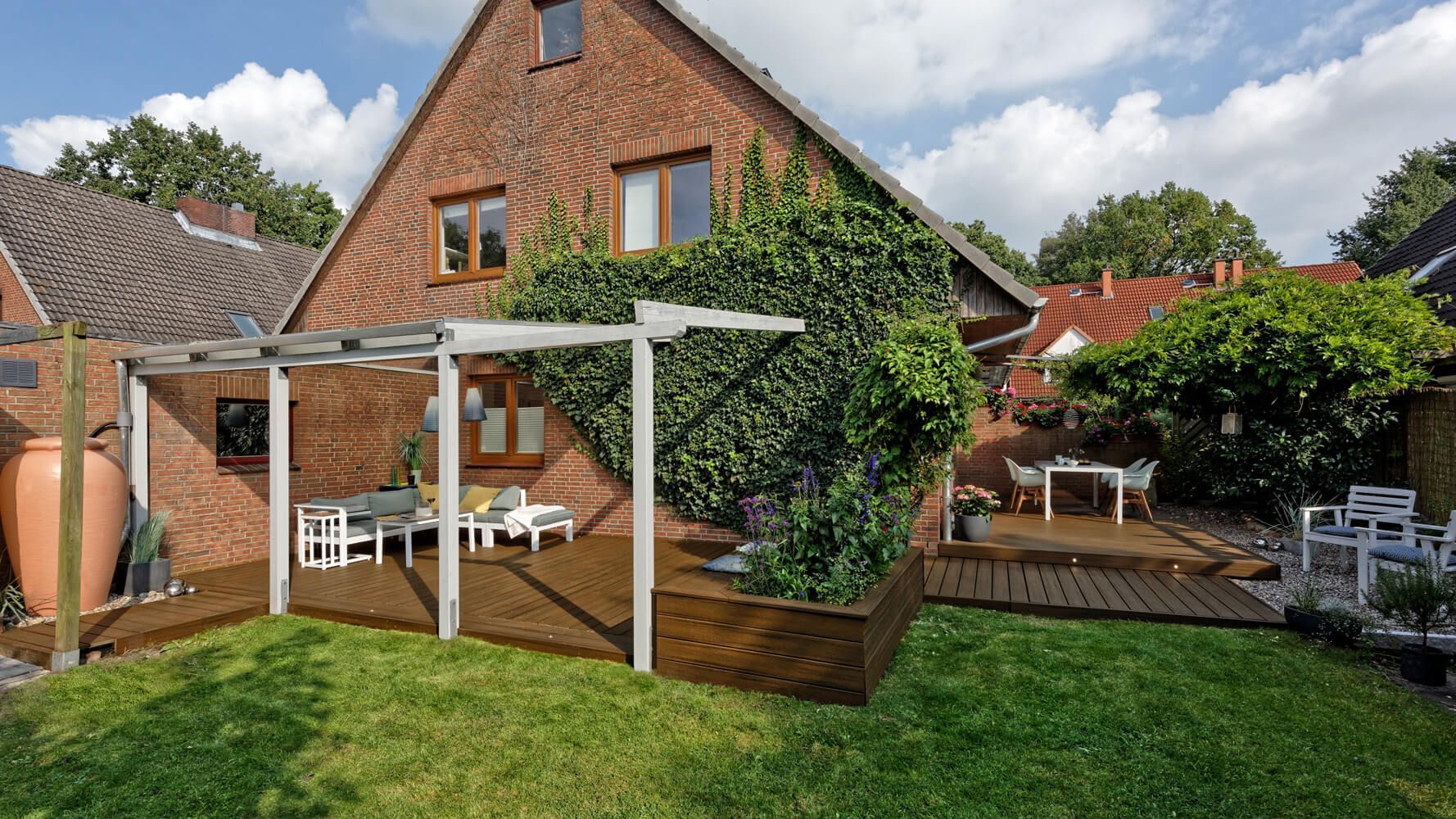 Klassisch gehaltene Terrasse ums Eck mit Überdachung und Pflanzkübel.